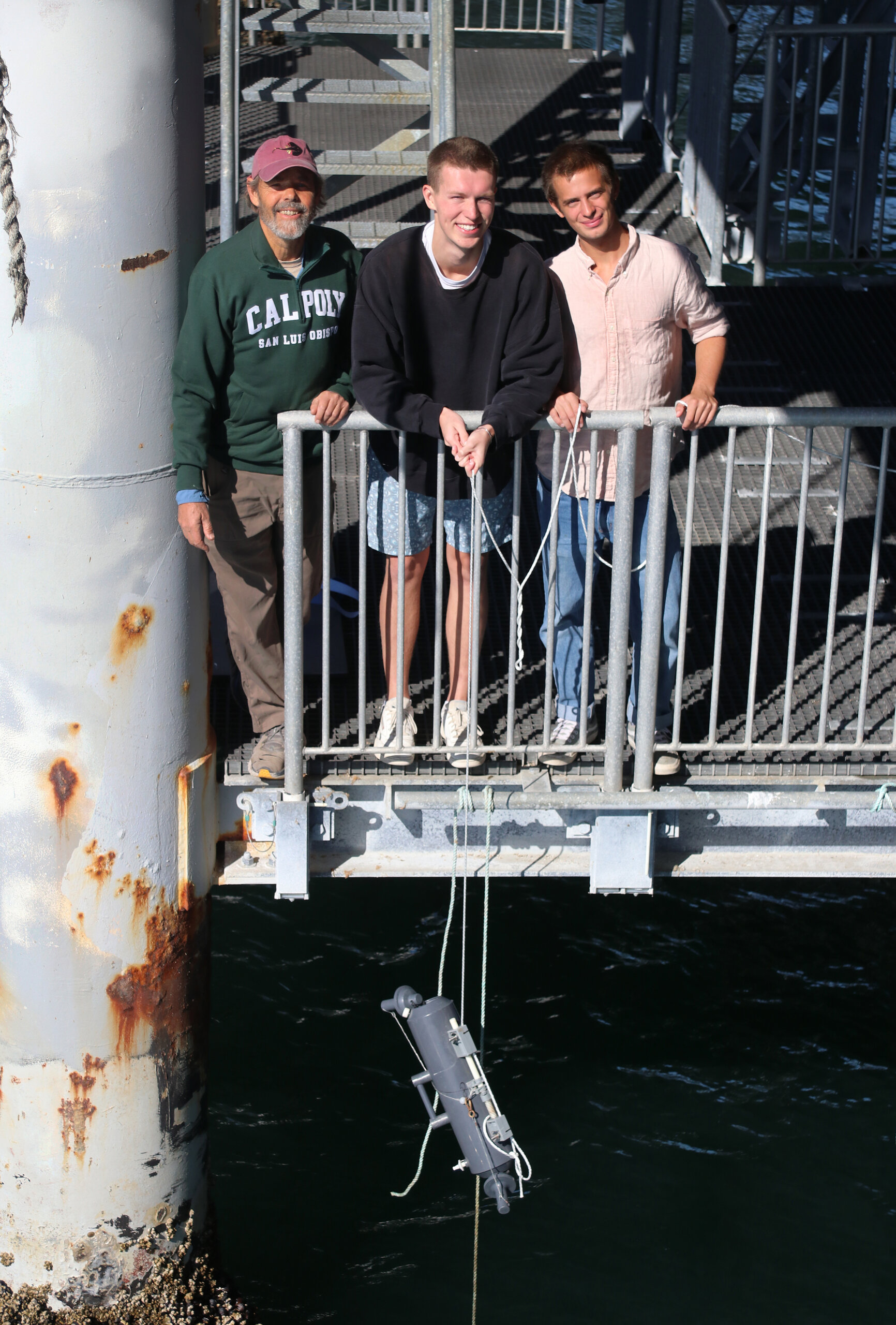 Professor and two students stand on the Cal Poly Research Pier while collecting ocean water 