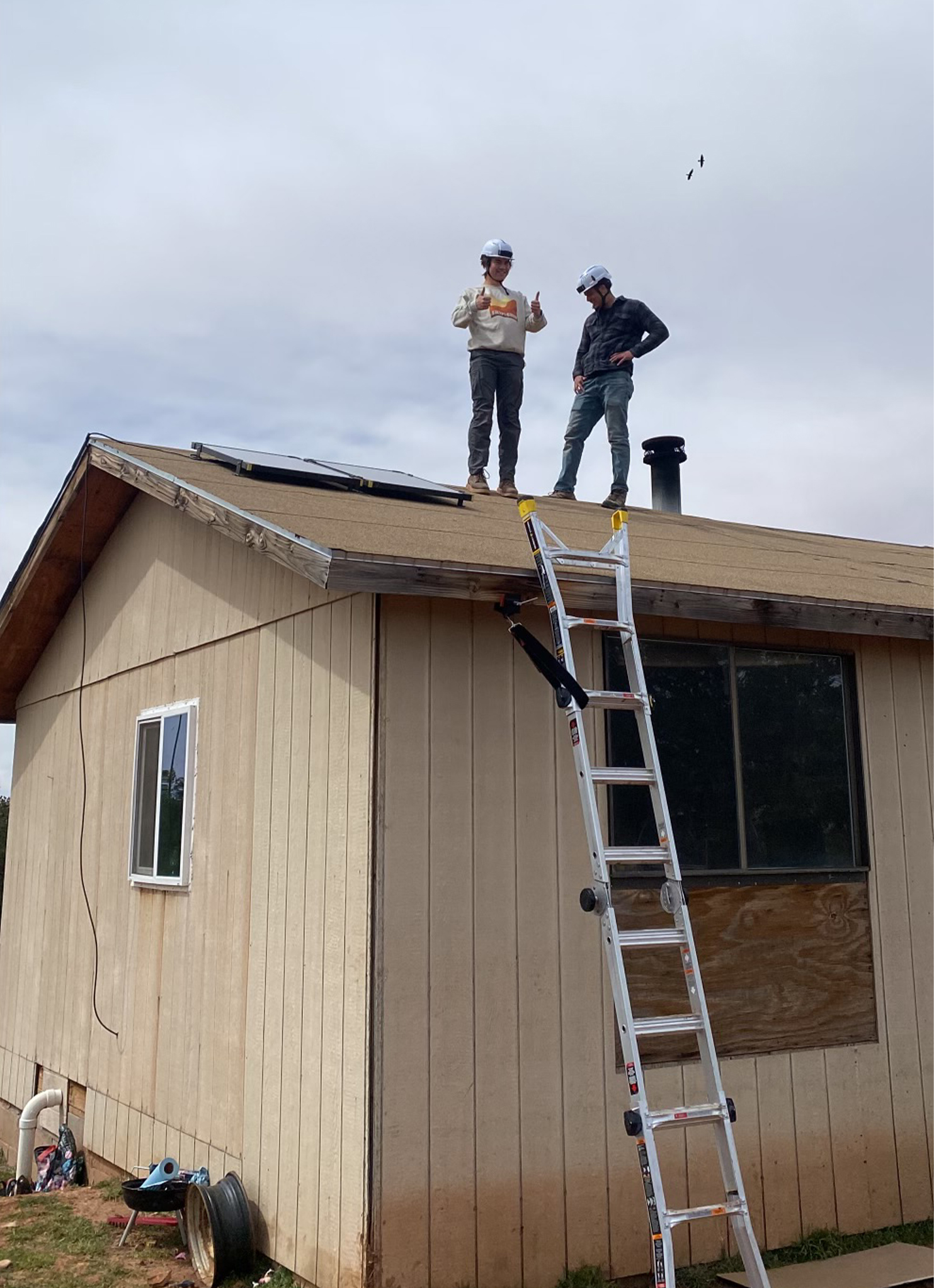 Two students install solar panels on roof