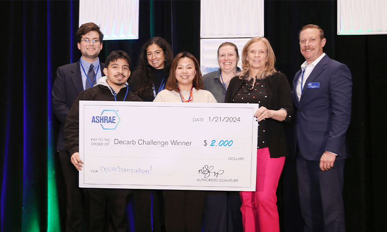 Seven people holding a giant check at a conference award ceremony.