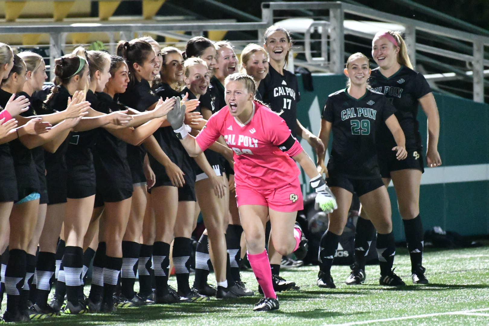 Cal Poly goalie Mac Samuel runs down the line of her teammates giving high-fives during a soccer game