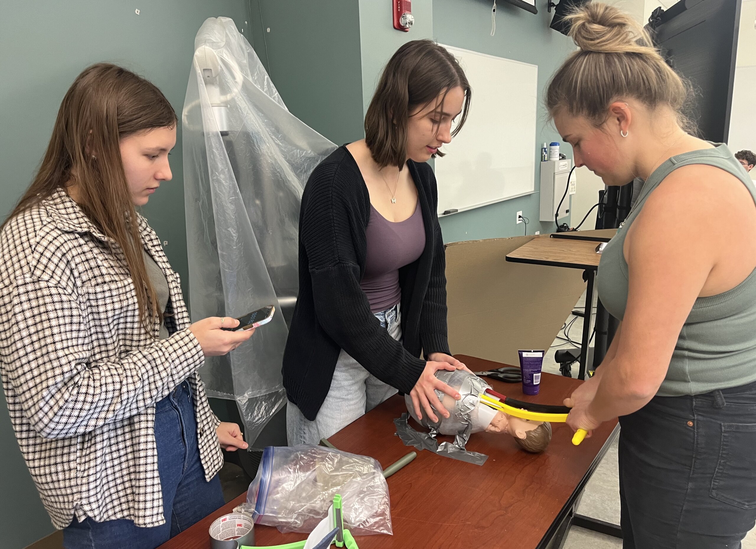 Three students simulate a delivery using a baby doll and giant plastic egg to test their assisted birth device