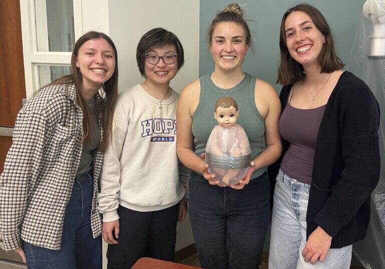 Senior project team of four students hold their baby doll and simulated uterus