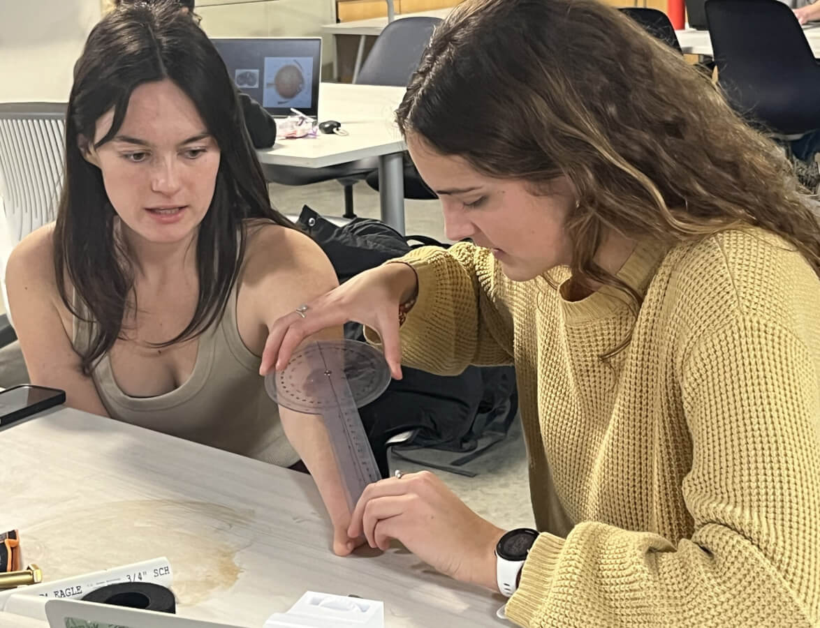 Student measures the arm of another student as they create a prosthetic device
