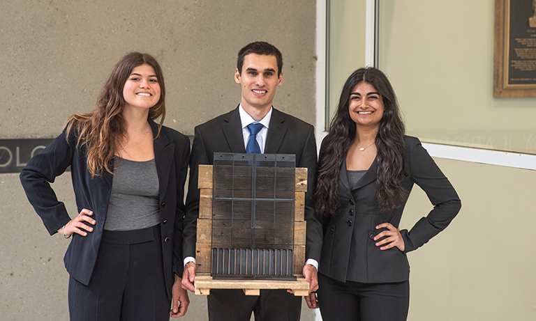 Three students holding up a wooden display with an object on it