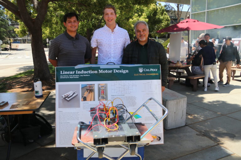 Two students and one faculty members standing behind a poster and a project prototype