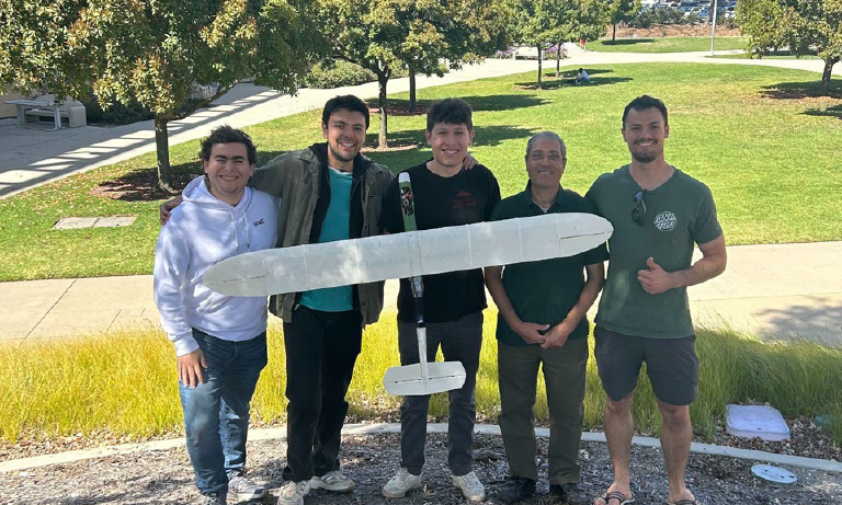 Five people holding a model aircraft and smiling at the camera