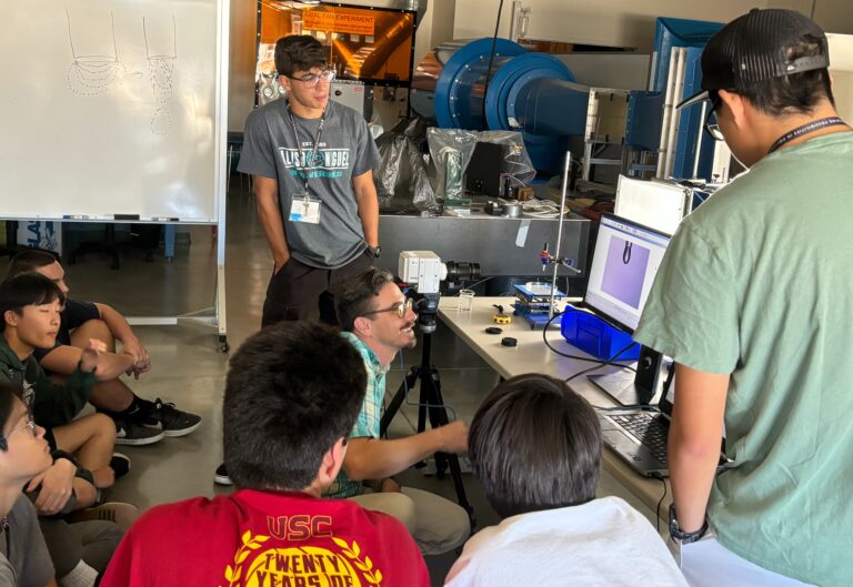 Students gather around professor and monitor with high-speed camera image or a water droplet