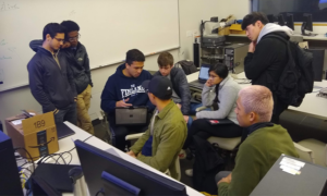 A group of students gathering around their classmate as he demonstrates a project.