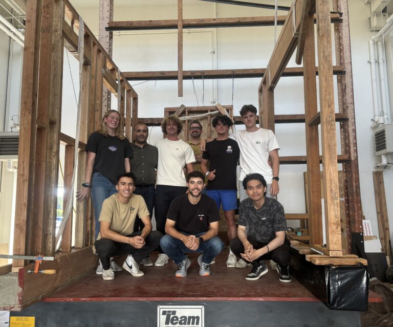 Students and faculty members stand on a shake table with part of their timber structure