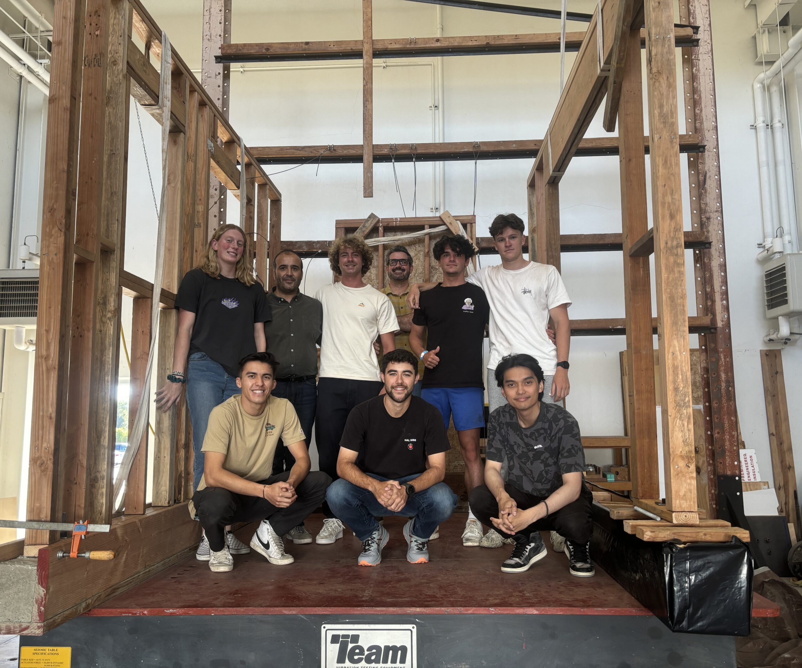 Students and faculty members stand on a shake table with part of their timber structure