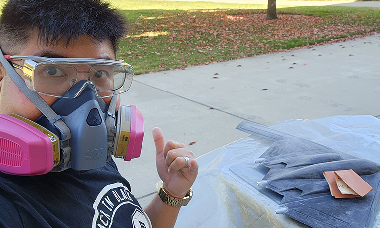 A man wearing safety glasses and pointing behind him at the work he's doing.