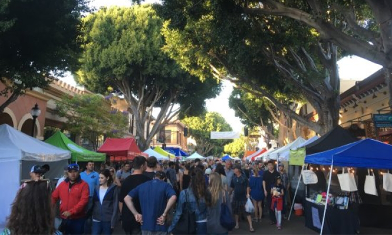 A group of people and vendor booths with tents at a farmers market.