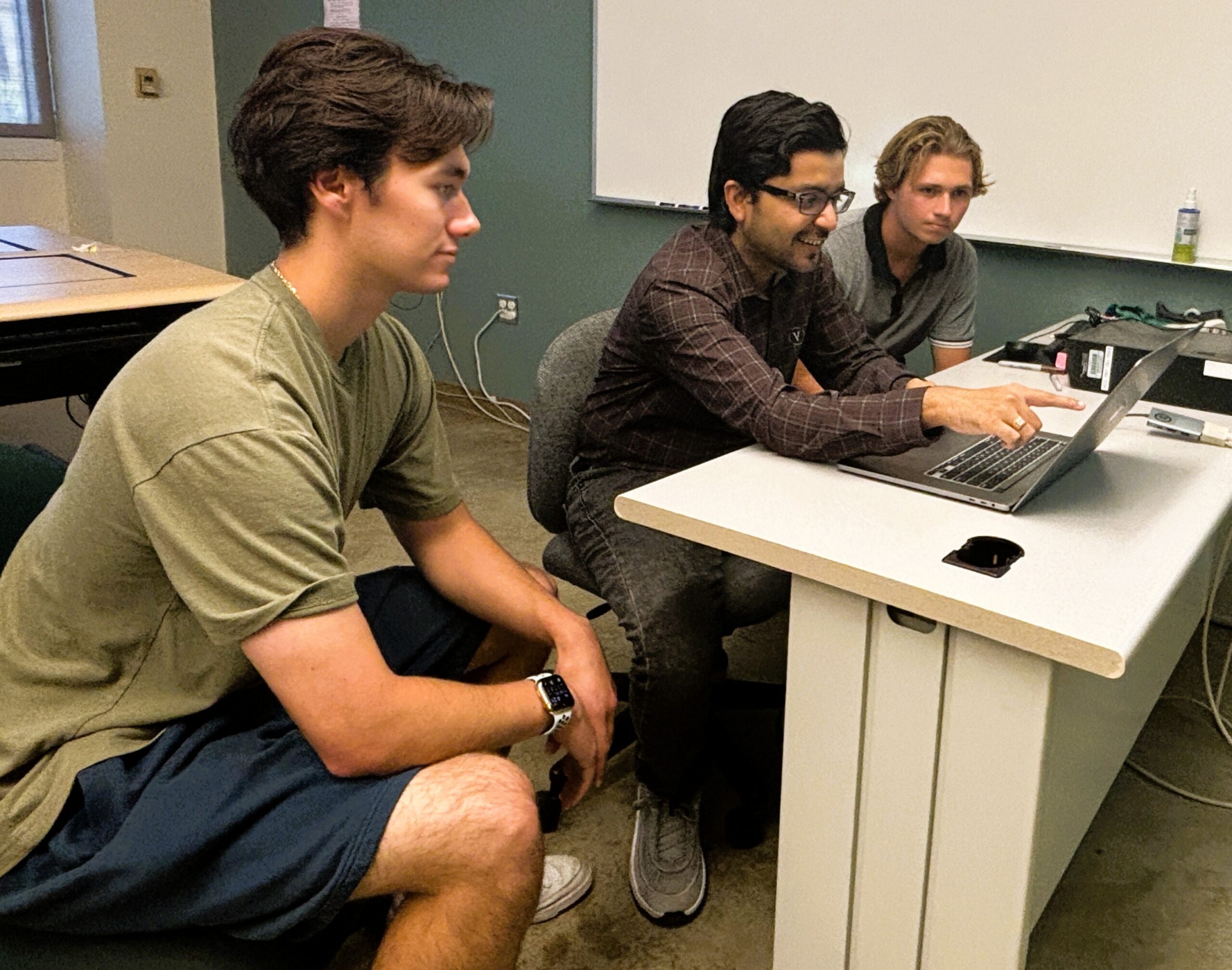 Professor works on laptop while students look on