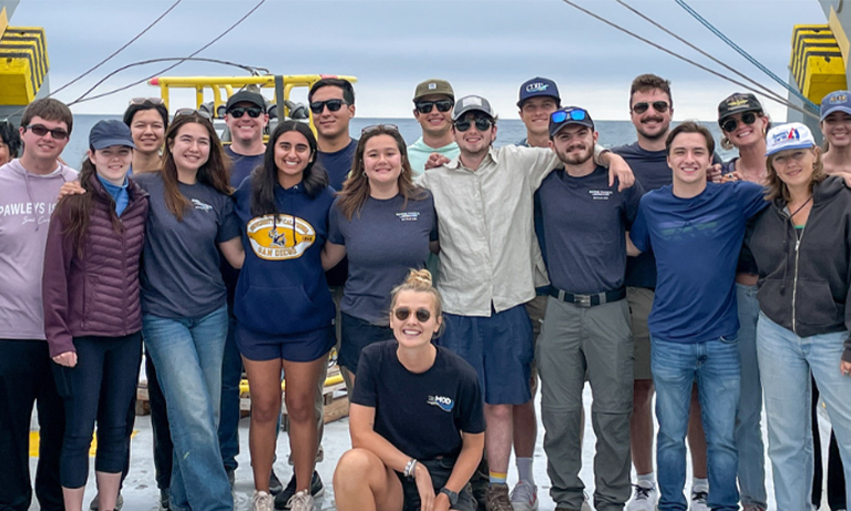 Students at the UCSD Marine Physical Laboratory Summer Internship Program on a dock with the ocean behind them.