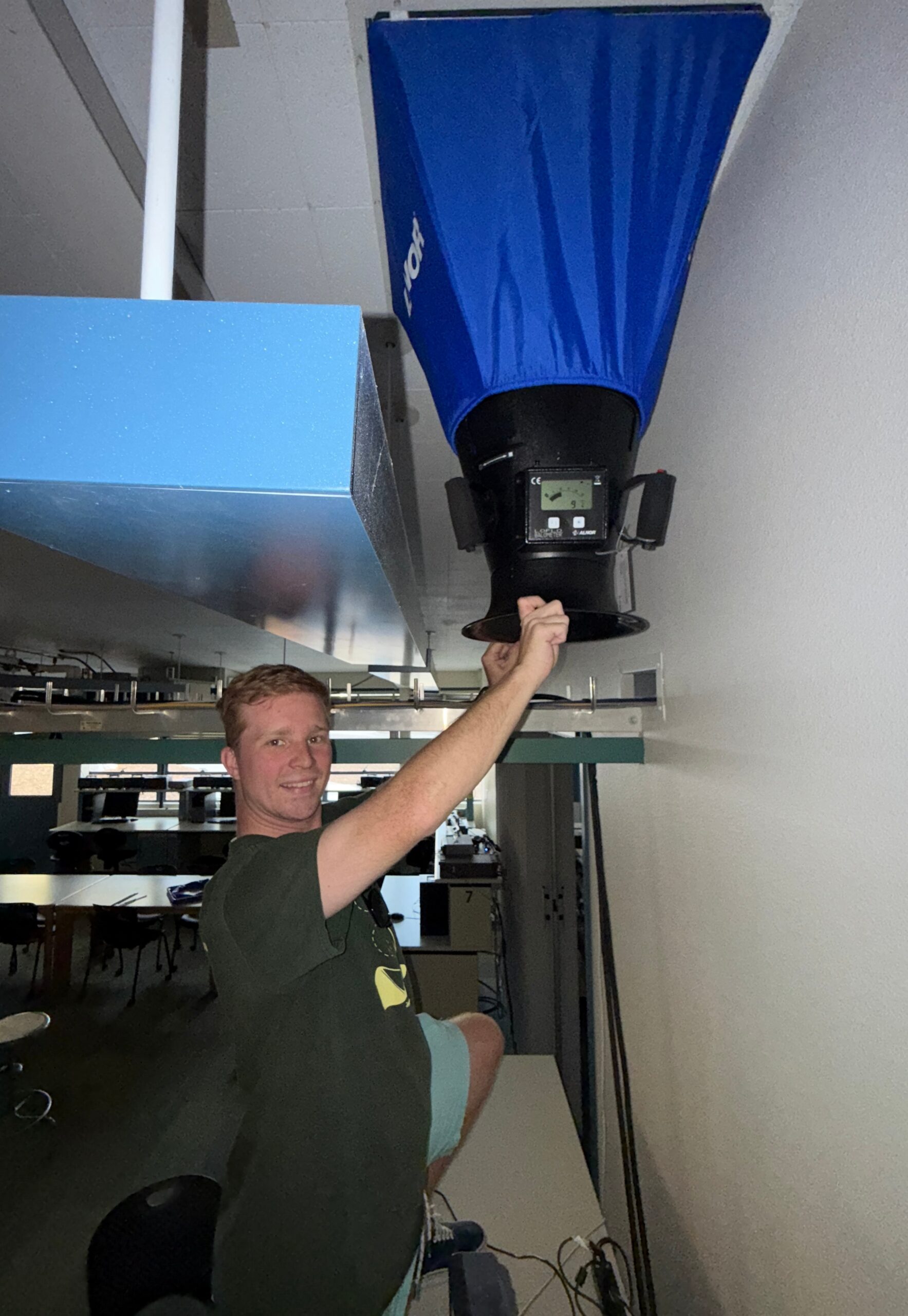 Andrew Sugamele measures airflow volume from a ceiling vent using a flow hood as part of his research on thermal comfort and ventilation in classrooms