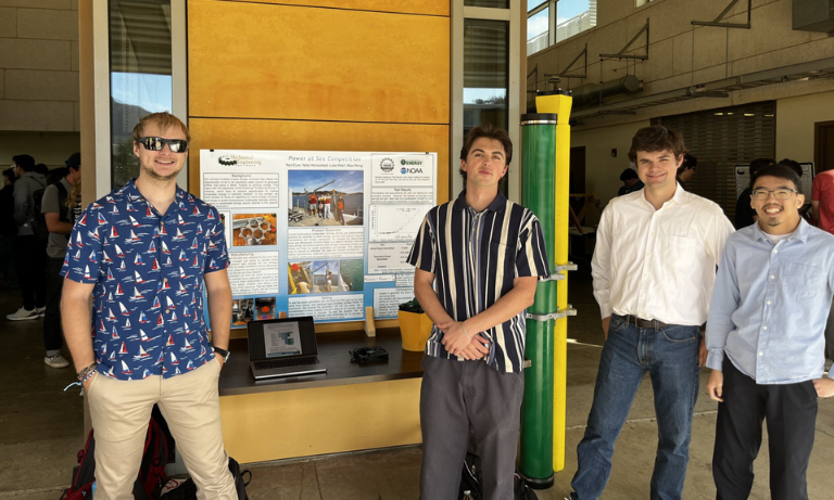 Four students standing in front of a research poster, all facing the camera and smiling.