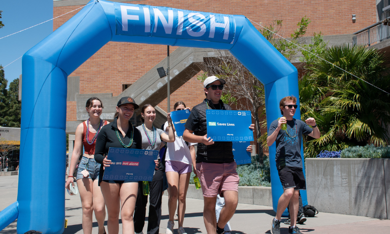 A group of people at a fundraiser walk holding up signs as they cross the finish line.