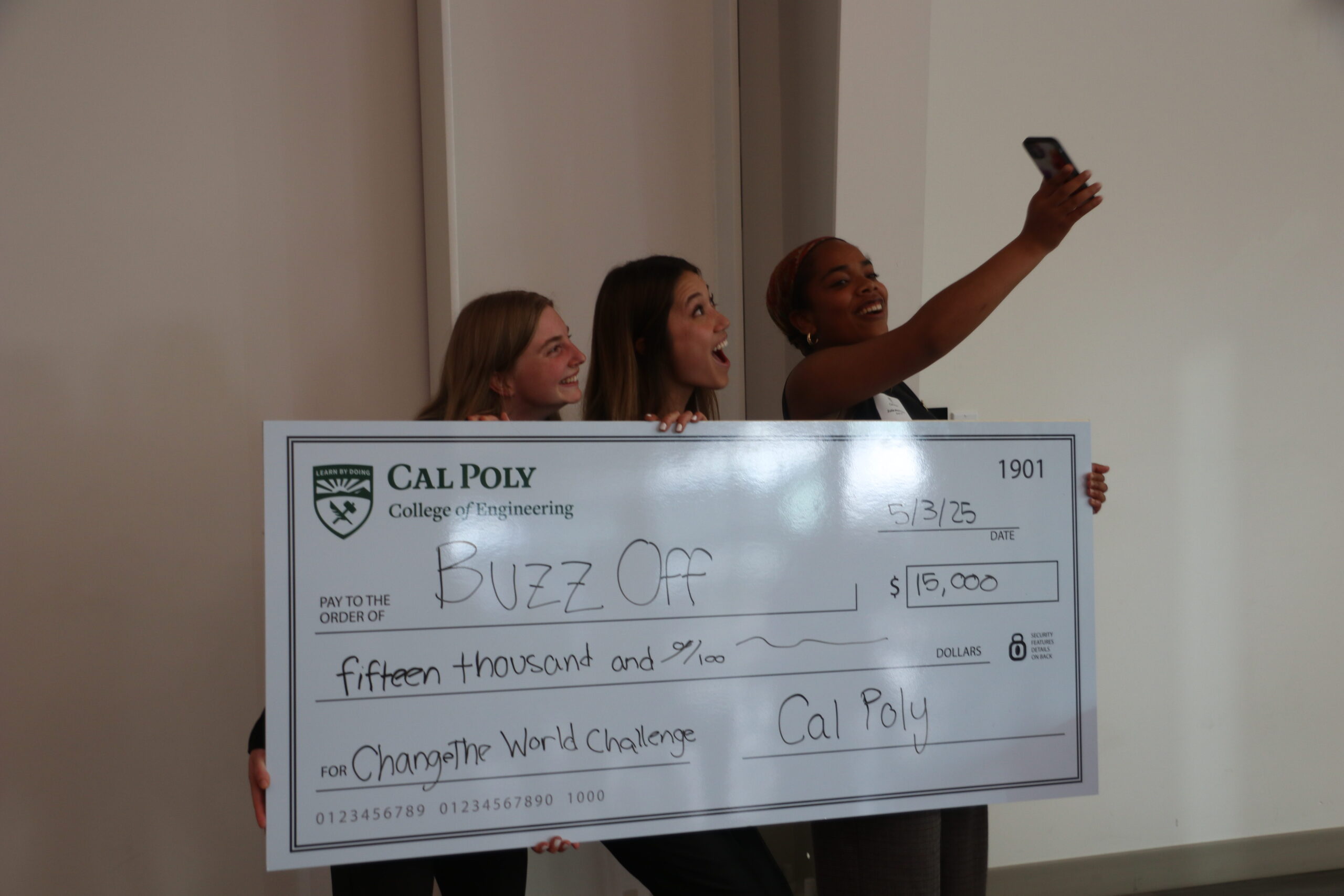 Three students taking a selfie with a giant check.