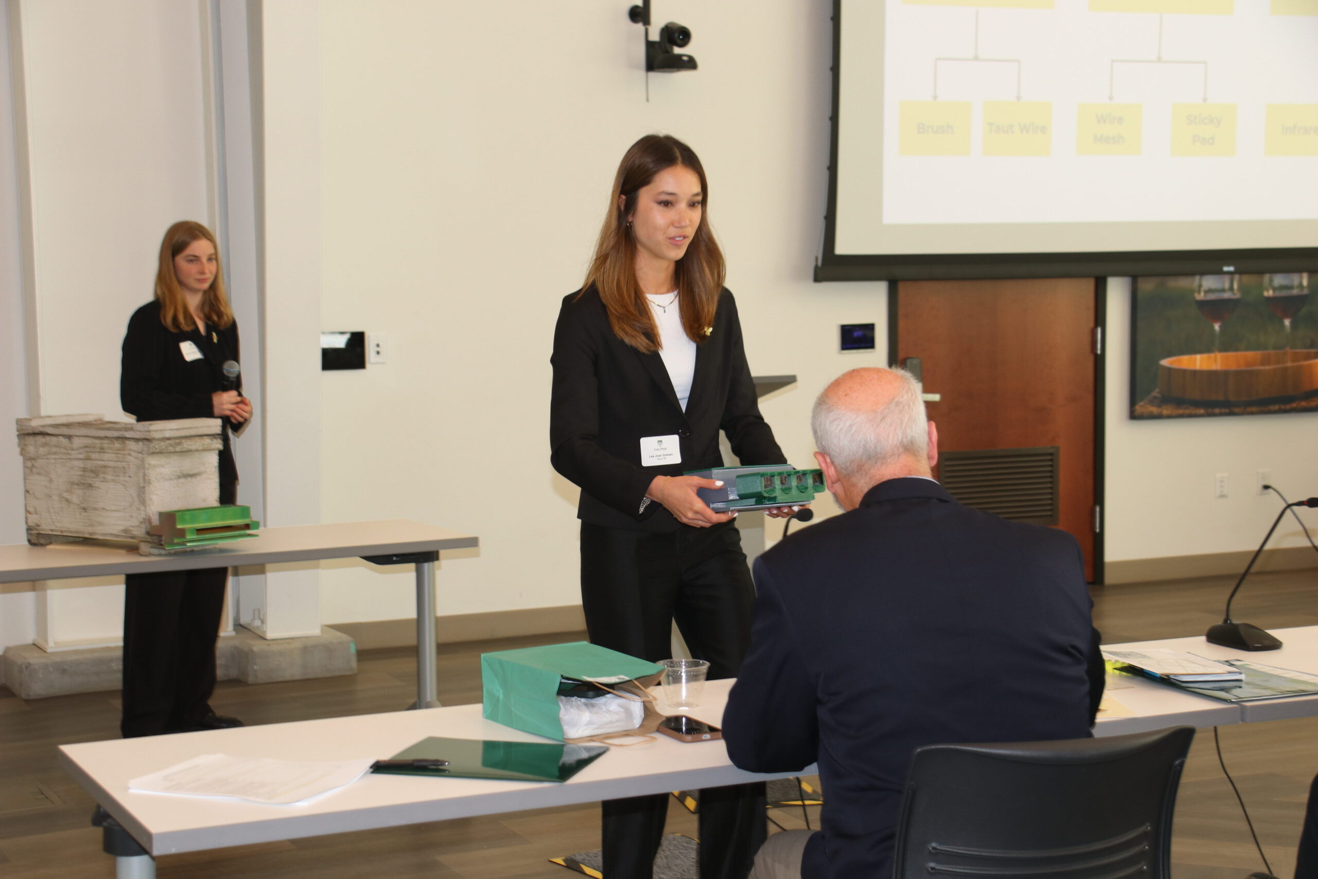 A student handing over a product prototype to a competition judge.