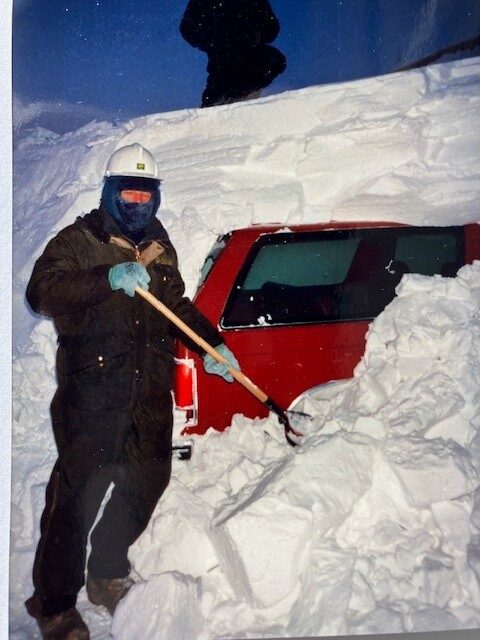A man shoveling snow that's covering a vehicle.