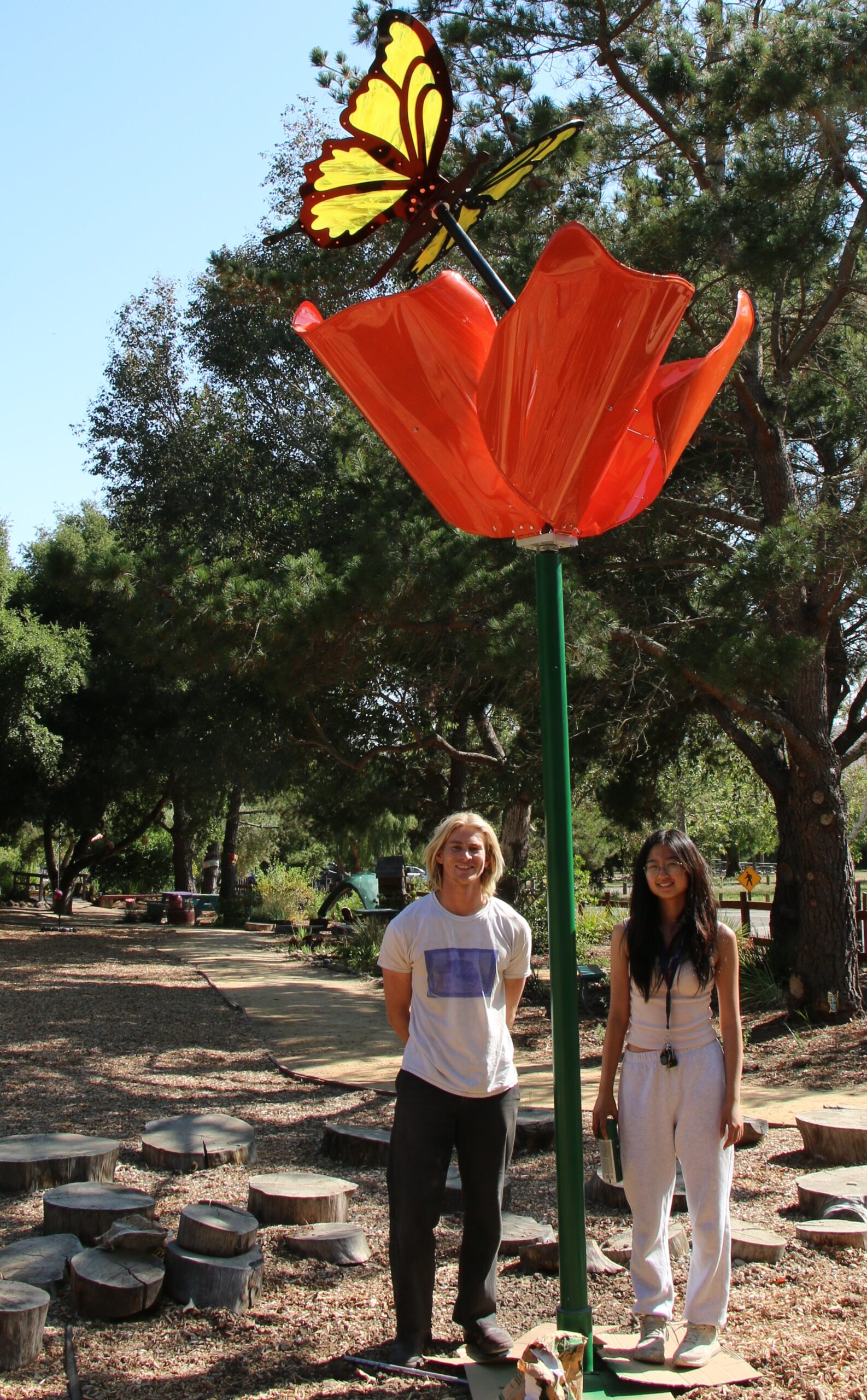 Students stand beneath their poppy and butterfly sculpture