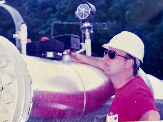 A man in a hard hat standing next to a large pipe