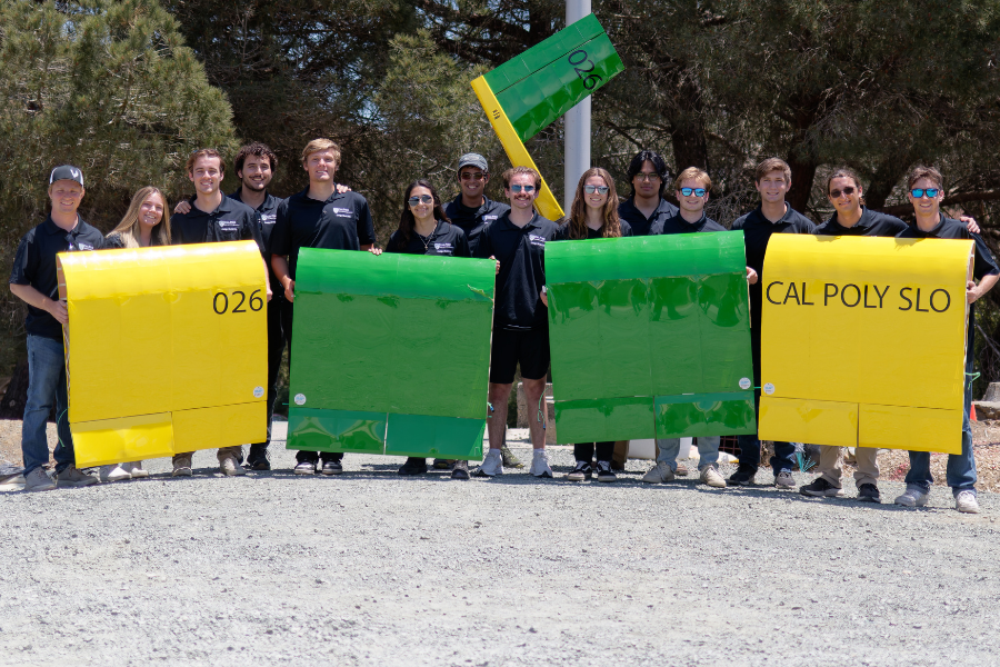Students in a row posing and holding up airplane parts.