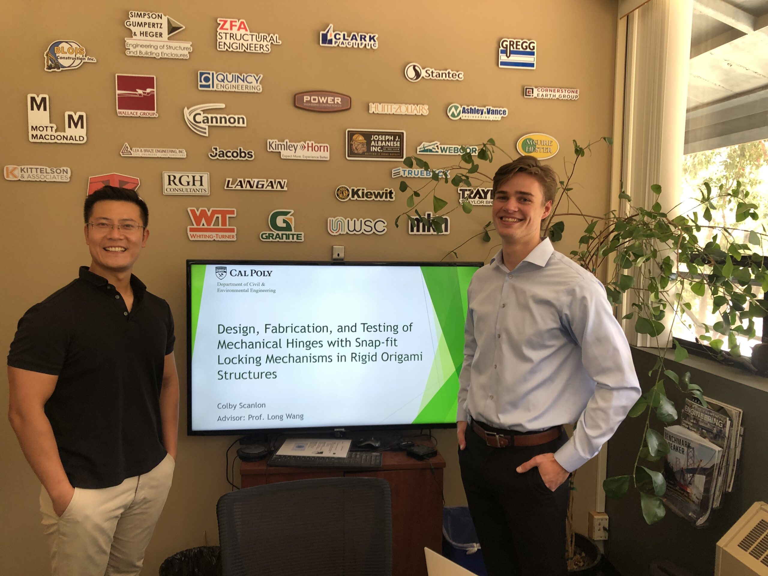 Professor and student stand in front of their presentation on a monitor