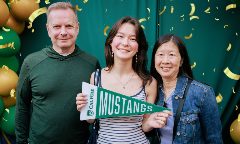 A Cal Poly student and her family posing in front of a festive green and gold background at Mustang Family Weekend