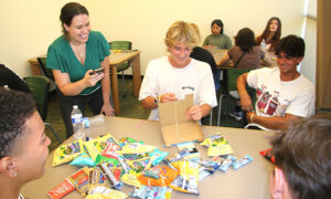 Professor times students using a "robot arm" made from cardboard to pick up snack packets.