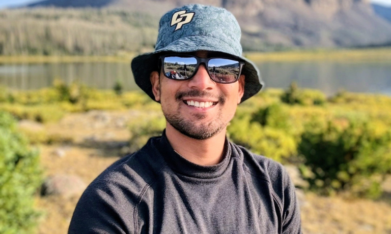 A man wearing a hat and sunglasses smiling at the camera