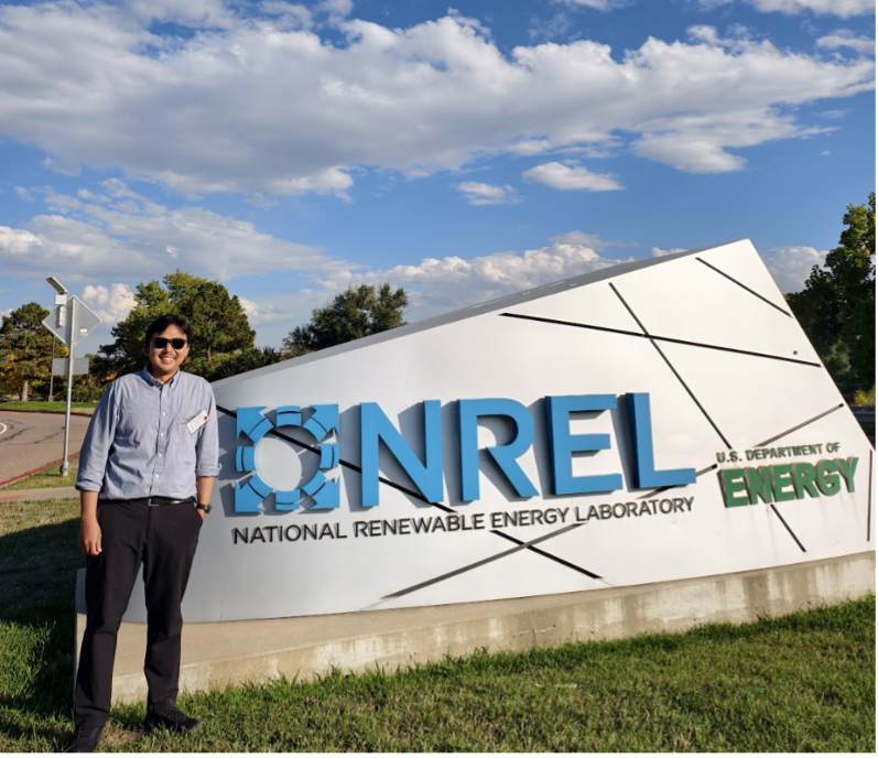 Visiting scholar stands next to sign designating the National Renewable Energy Laboratory
