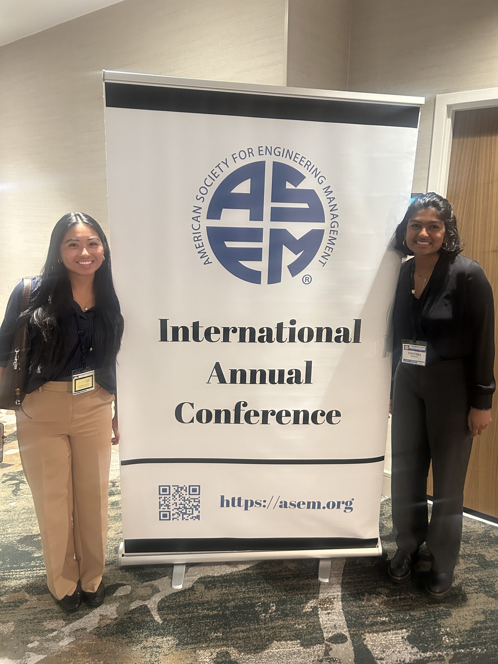 Two women in business attire standing by a conference sign