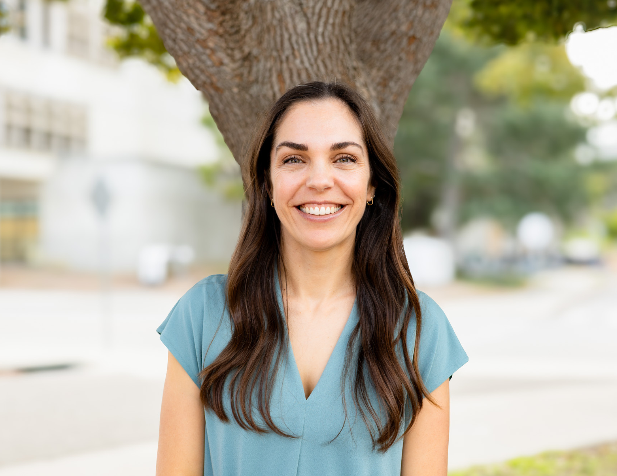 A woman standing smiling in front of a tree