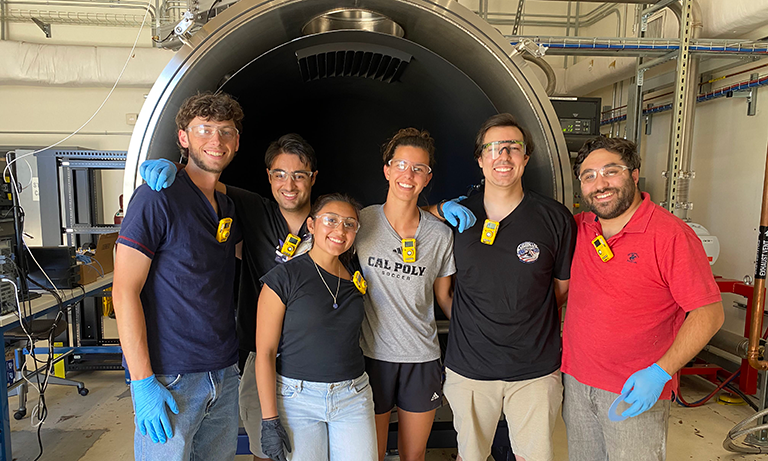Team of students stand in front of the TVAC